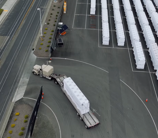 White crates in a sotrage yard, with one being driven out of the complex on a semi trailer
